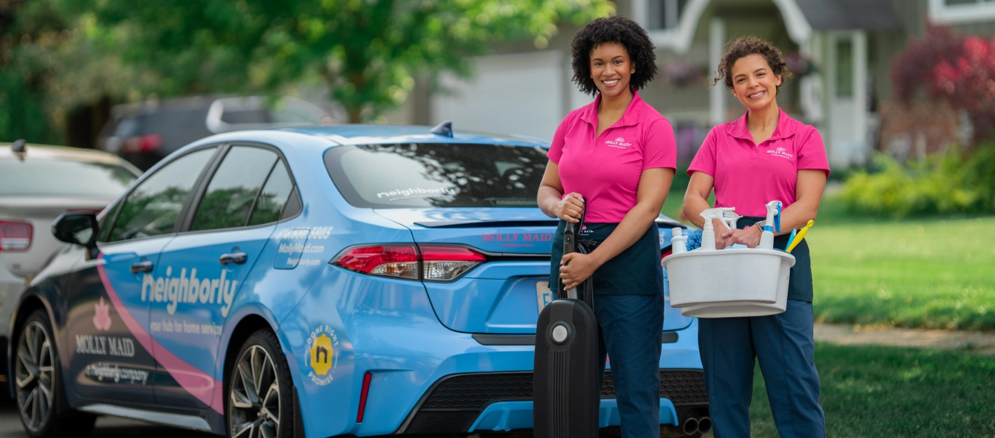 Molly Maid house cleaning pros standing outside home with cleaning supplies