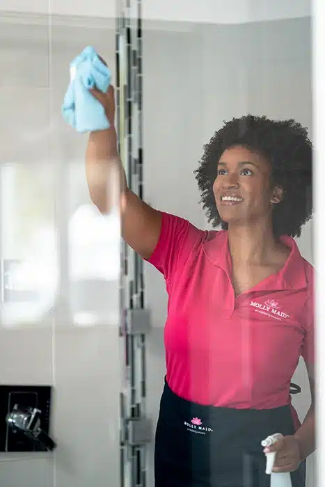A Molly Maid professional wiping a shower door at a move-out cleaning appointment 